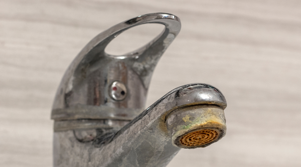 A chrome bathroom faucet tap heavily coated with dull white limescale stains and yellowish hard water mineral crust buildup around the aerator nozzle