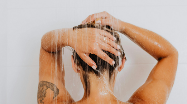 Back view of a woman washing her hair under a bathroom shower stream that contains hidden chlorine minerals and hard water impurities