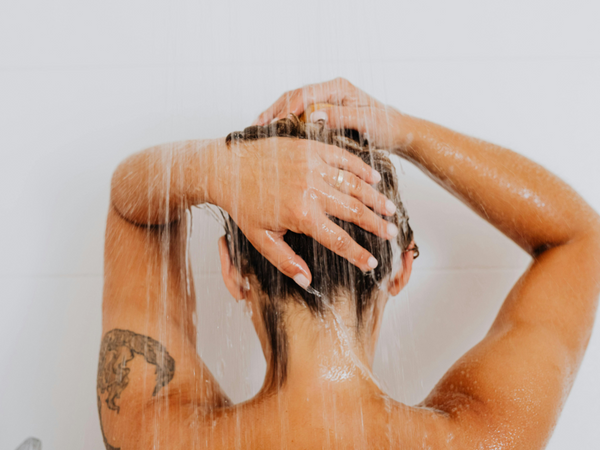 Back view of a woman washing her hair under a bathroom shower stream that contains hidden chlorine minerals and hard water impurities