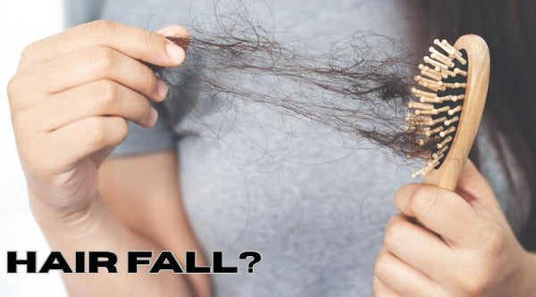 A woman holding a wooden hairbrush filled with loose hair strands alongside the graphic text banner reading HAIR FALL to illustrate hard water breakage symptoms