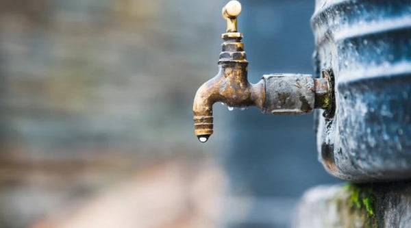 An old brass outdoor water tap faucet connected to a domestic storage tank leaking unrefined groundwater rich in hair fall causing minerals