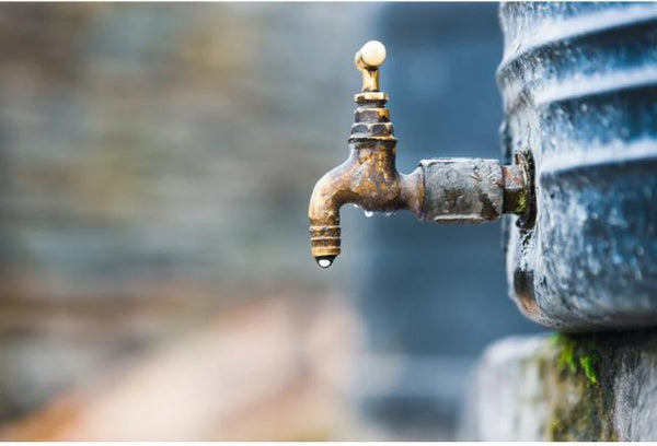An old brass outdoor water tap faucet connected to a domestic storage tank leaking unrefined groundwater rich in hair fall causing minerals