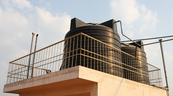 Two large black plastic domestic overhead water storage tanks installed on a residential rooftop concrete terrace setup for whole house water supply distribution