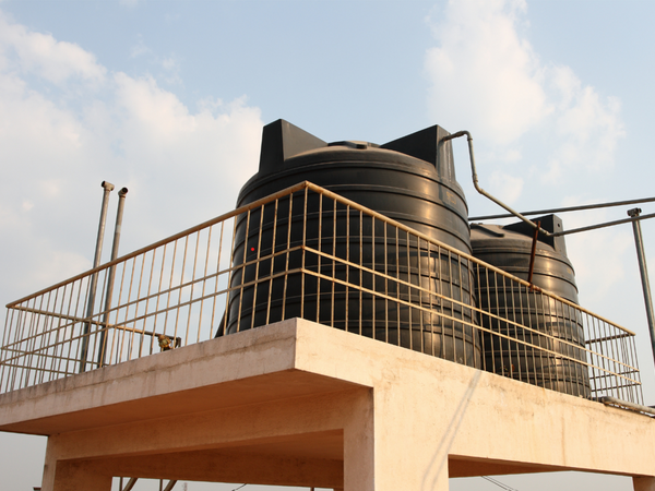 Two large black plastic domestic overhead water storage tanks installed on a residential rooftop concrete terrace setup for whole house water supply distribution