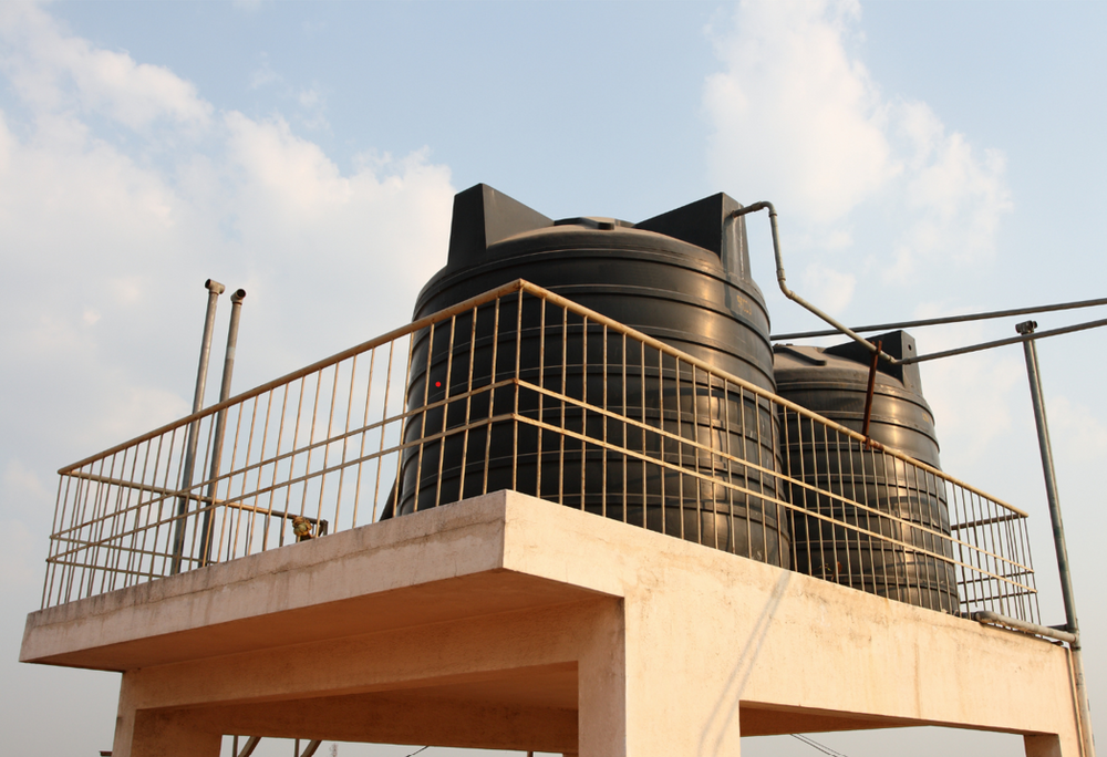 Two large black plastic domestic overhead water storage tanks installed on a residential rooftop concrete terrace setup for whole house water supply distribution