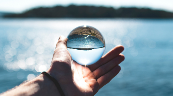 A person holding a clear glass crystal ball over a blue ocean horizon symbolizing a clear perspective on analyzing water purity and total dissolved solids metrics