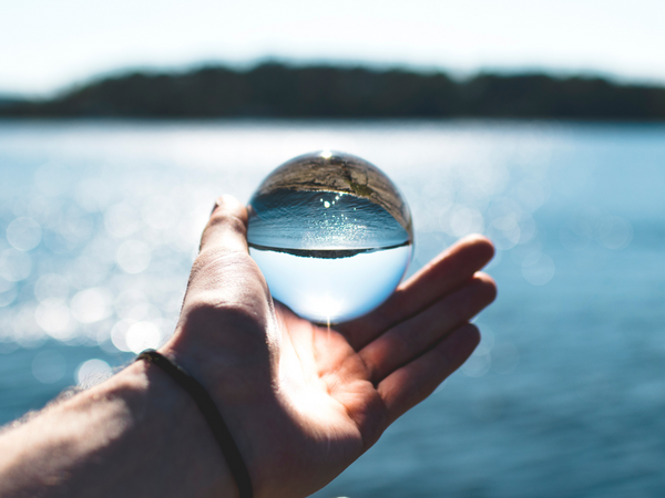 A person holding a clear glass crystal ball over a blue ocean horizon symbolizing a clear perspective on analyzing water purity and total dissolved solids metrics