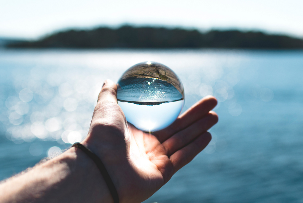 A person holding a clear glass crystal ball over a blue ocean horizon symbolizing a clear perspective on analyzing water purity and total dissolved solids metrics